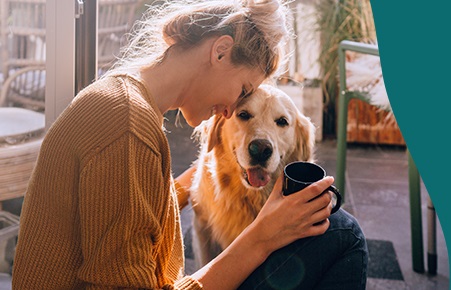 Jonge vrouw met kop koffie in haar hand knuffelt haar hond